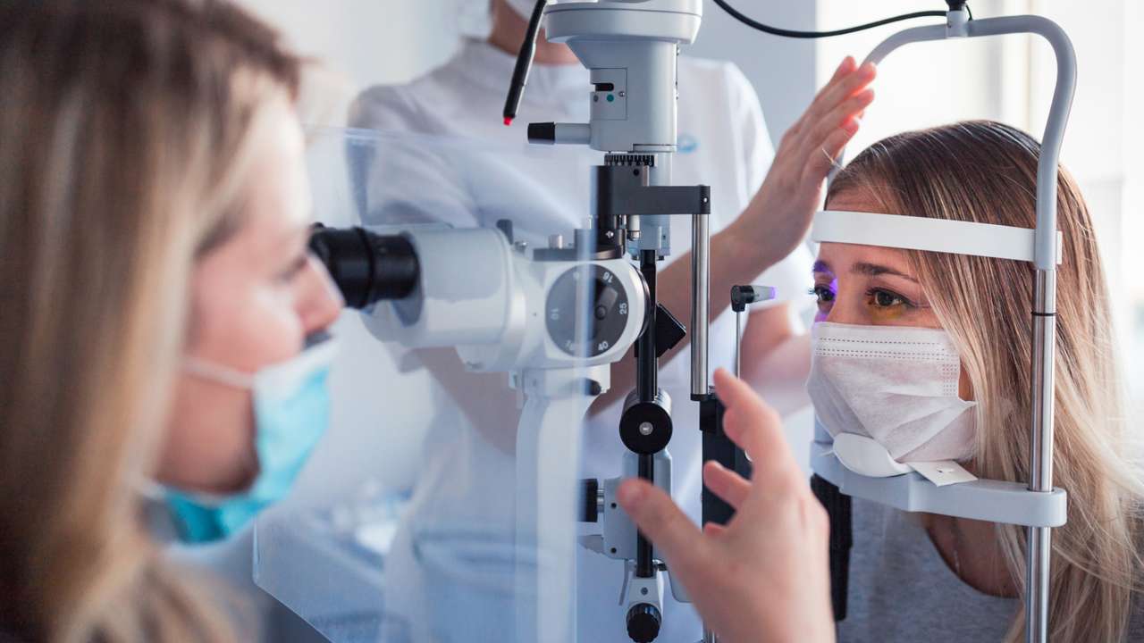 Young woman wearing a medical protective mask when having eye pressure measured at the ophthalmologist