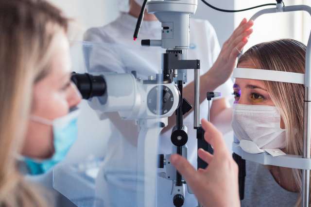 Young woman wearing a medical protective mask when having eye pressure measured at the ophthalmologist