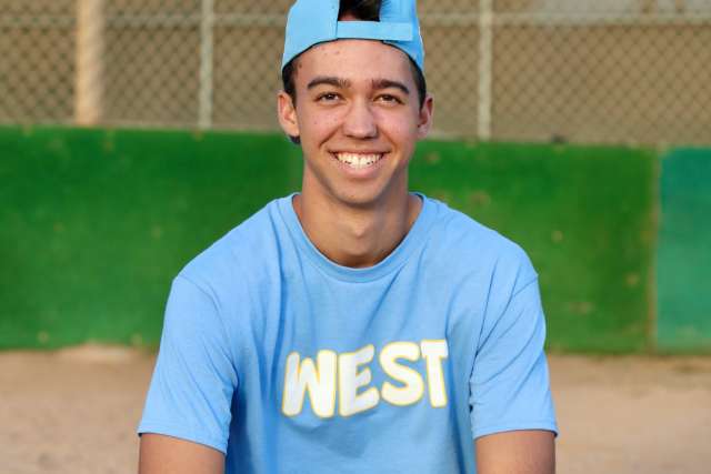 Adolescent male sitting on baseball field.