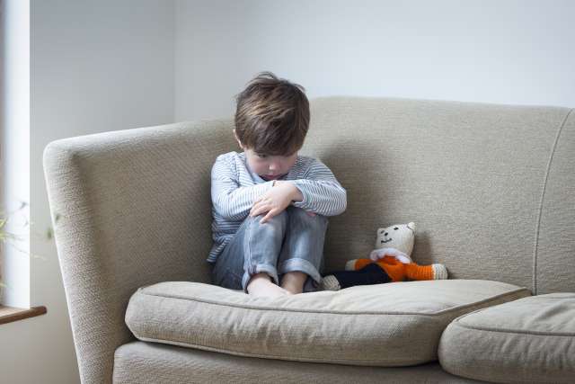 Little boy suffering from child abuse curled up on the sofa with his teddy bear.