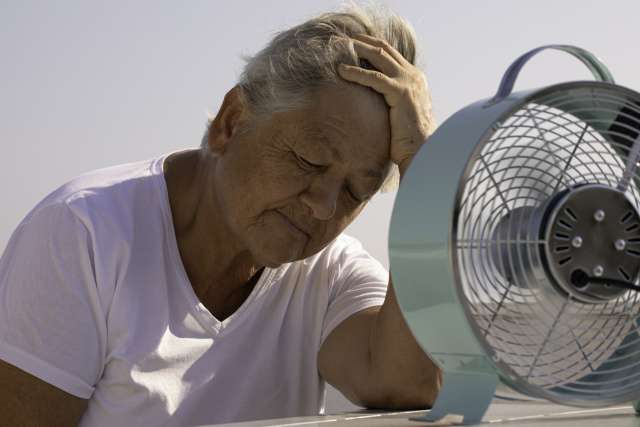 A woman sits by a fan to cool off.