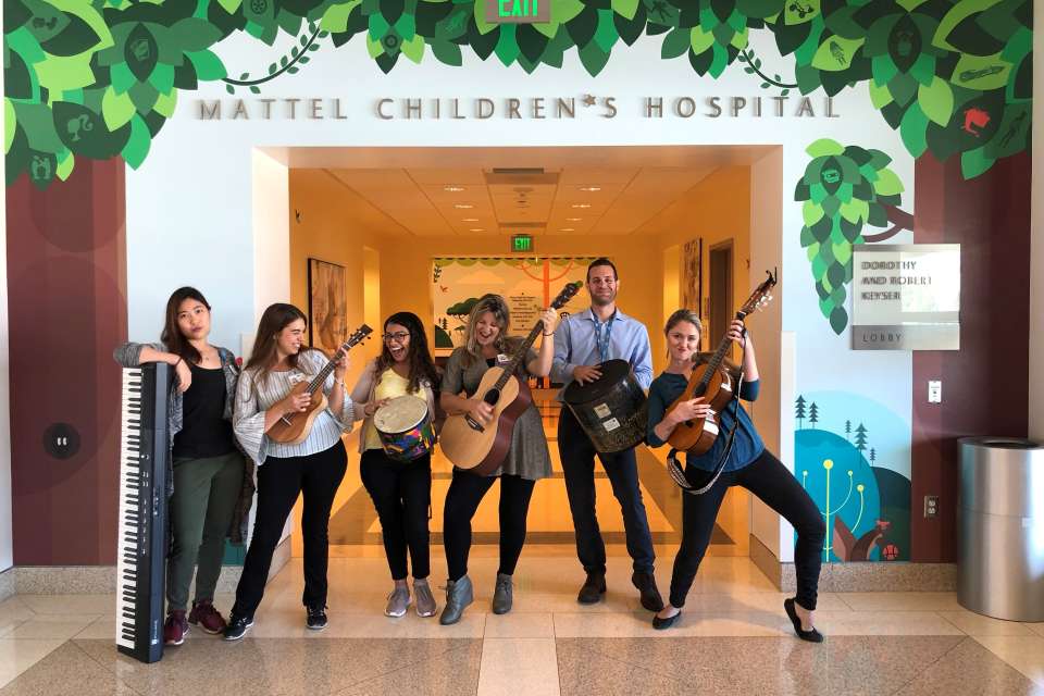 Group of Music Therapy musicians posing with their instruments underneath Mattel Children's Hospital sign