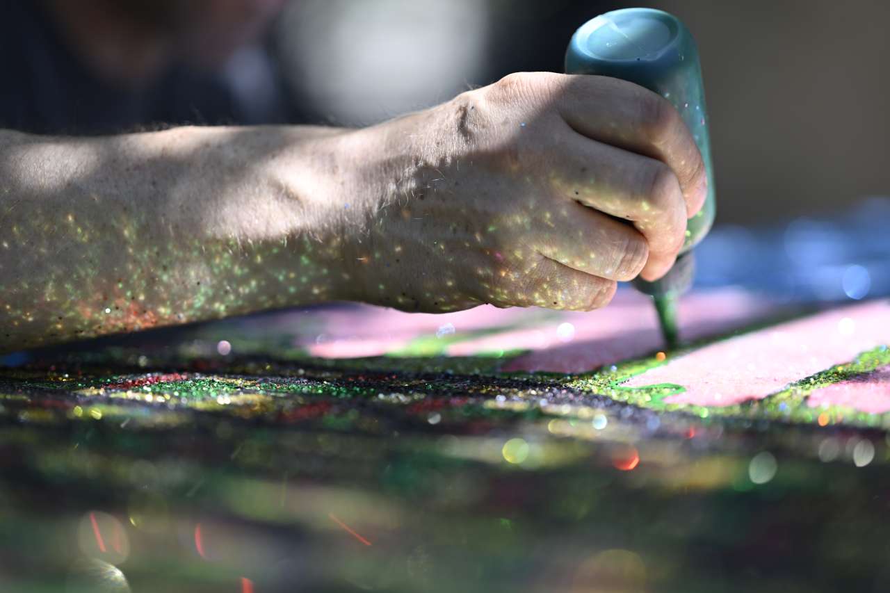 Dylan Mortimer's right arm is covered with glitter as he works on a painting.