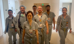 A group of seven healthcare professionals dressed in scrubs walk confidently in a hospital corridor.