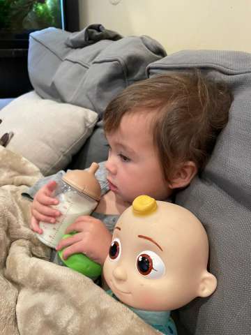 Christine Nguyen-Buckley, MD shares photo of son, Christopher Buckley, holding bottle of milk sitting next to Cocomelon "JJ" Doll