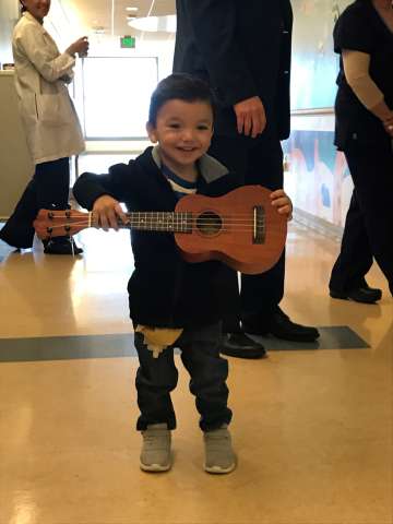 Young boy holding a small guitar and smiling