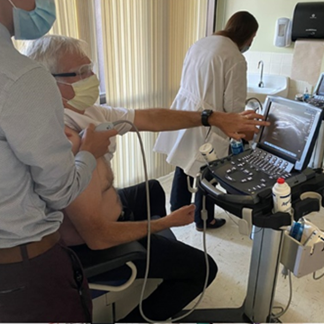 A man wearing a mask and glasses points at an image on an ultrasound machine.